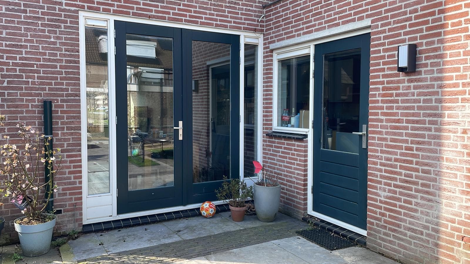 Geschilderde kozijnen en deuren in donkergroen en crème aan een bakstenen woning